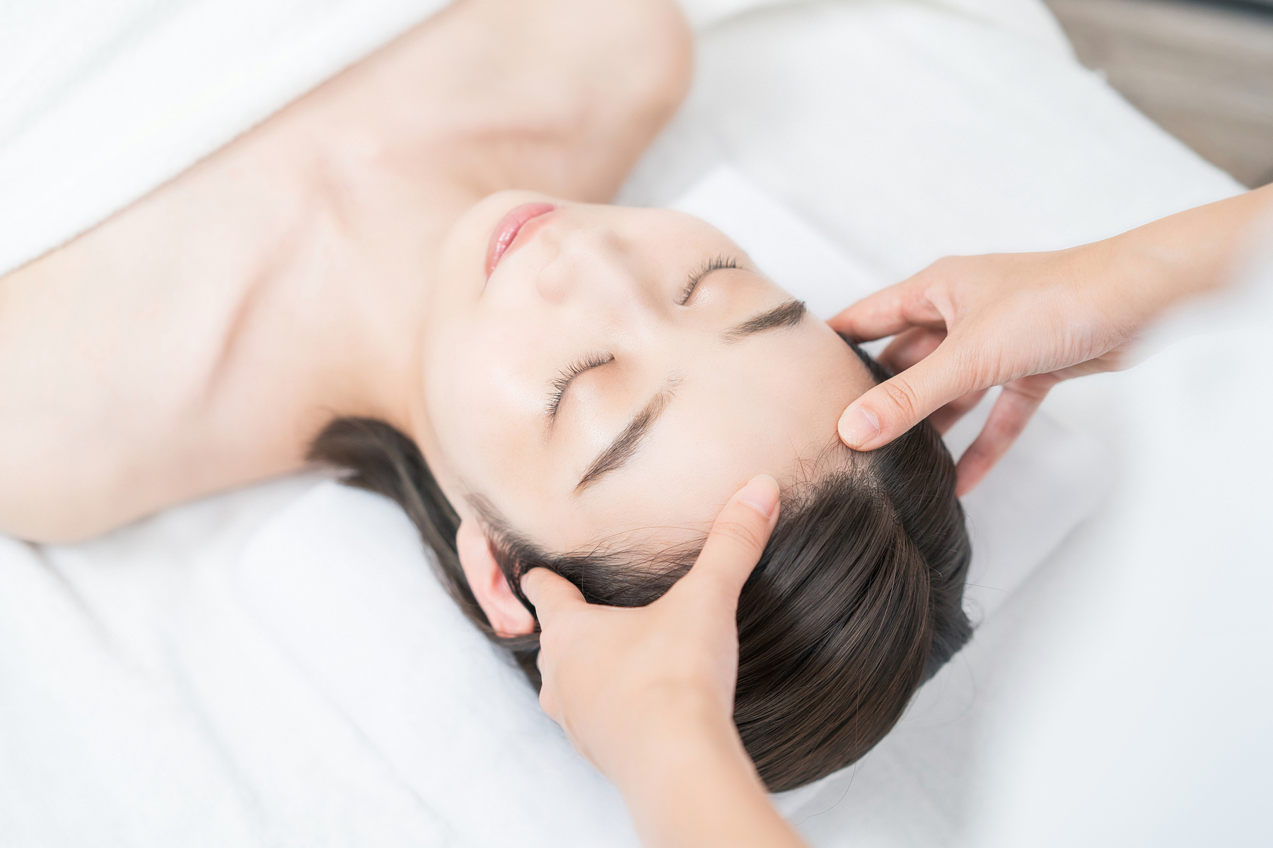 A young woman whose head is massaged at an esthetic salon